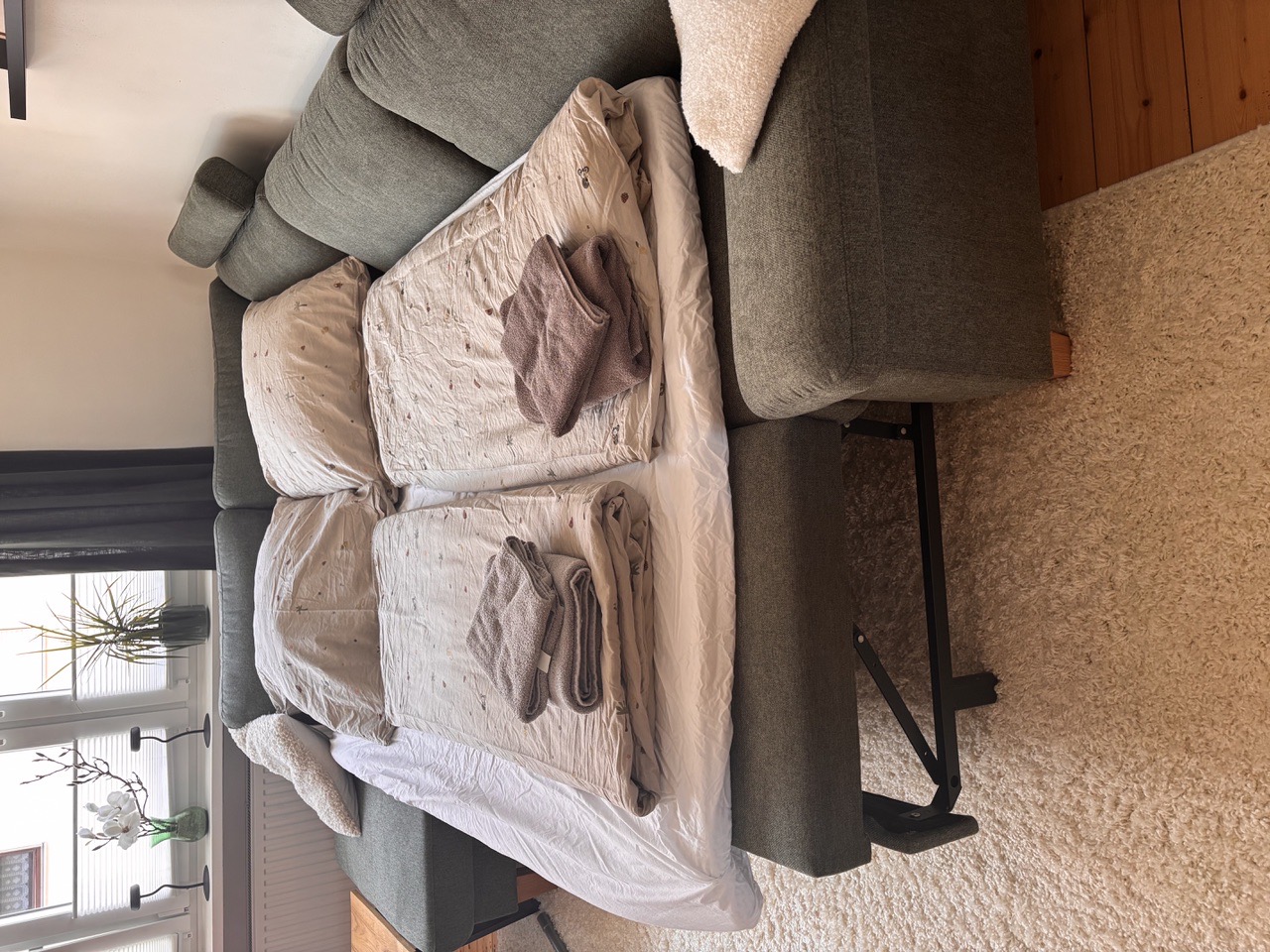 Ausgeklapptes Schlafsofa im Wohnzimmer mit frischer Bettwäsche und Handtüchern